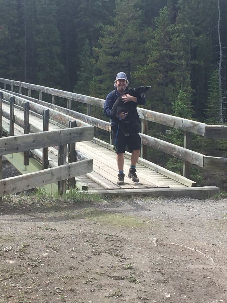 Man carrying dog over a scary wooden bridge