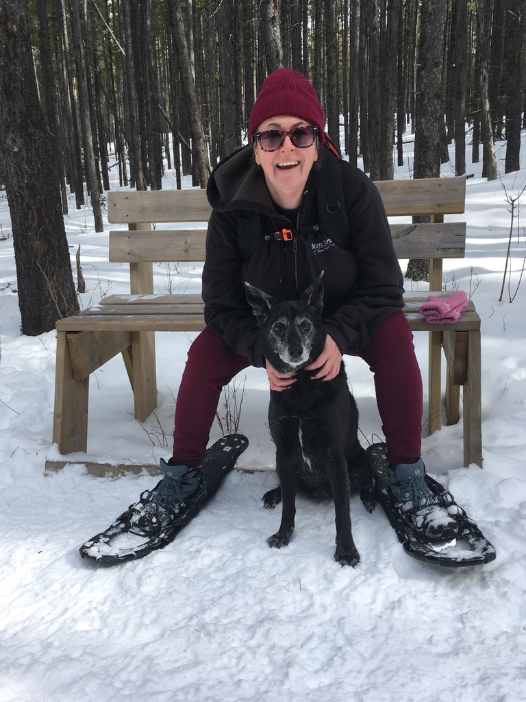 Woman in snowshoes sitting on a bench with a dog